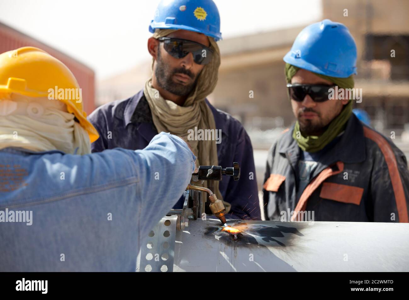 Schweißer, die beim Bau einer großen Ölanlage in der Wüste Sahara mit einem Gasbrenner Rohre schneiden. Stockfoto