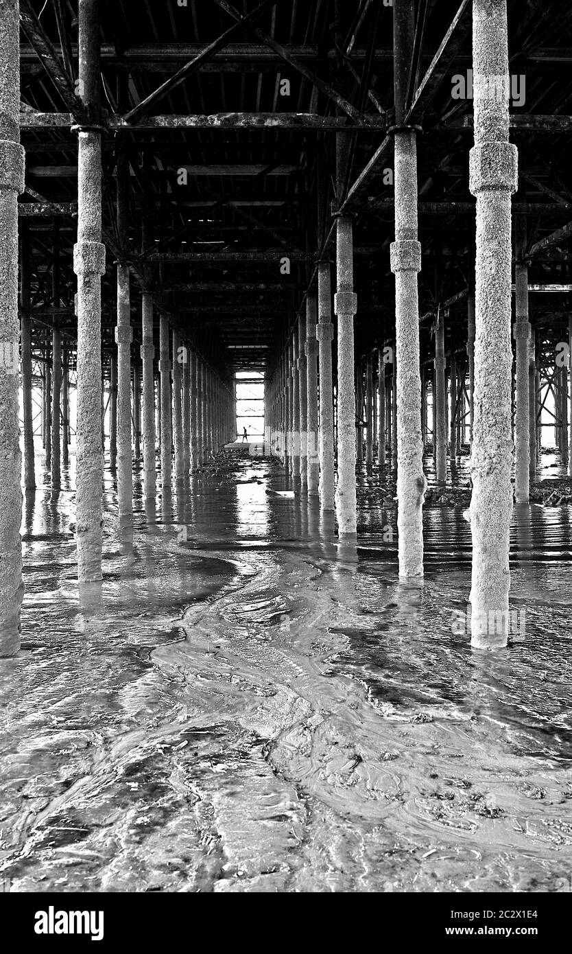 Unter dem Pier bei Ebbe mit Silhouette der Figur in der Ferne Stockfoto