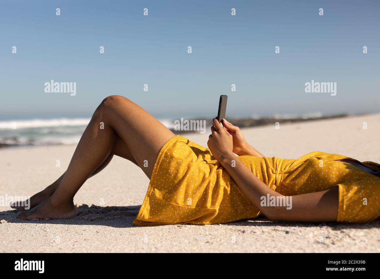 Mixed Race Frau mit Smartphone am Strand Stockfoto