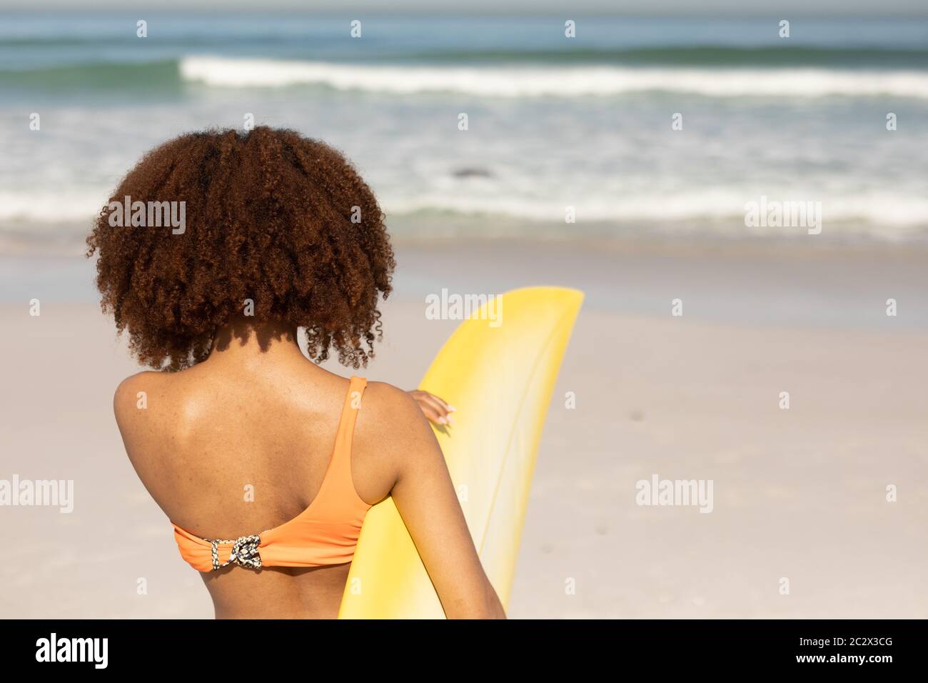 Mixed Race Frau hält Surfbrett am Strand Stockfoto