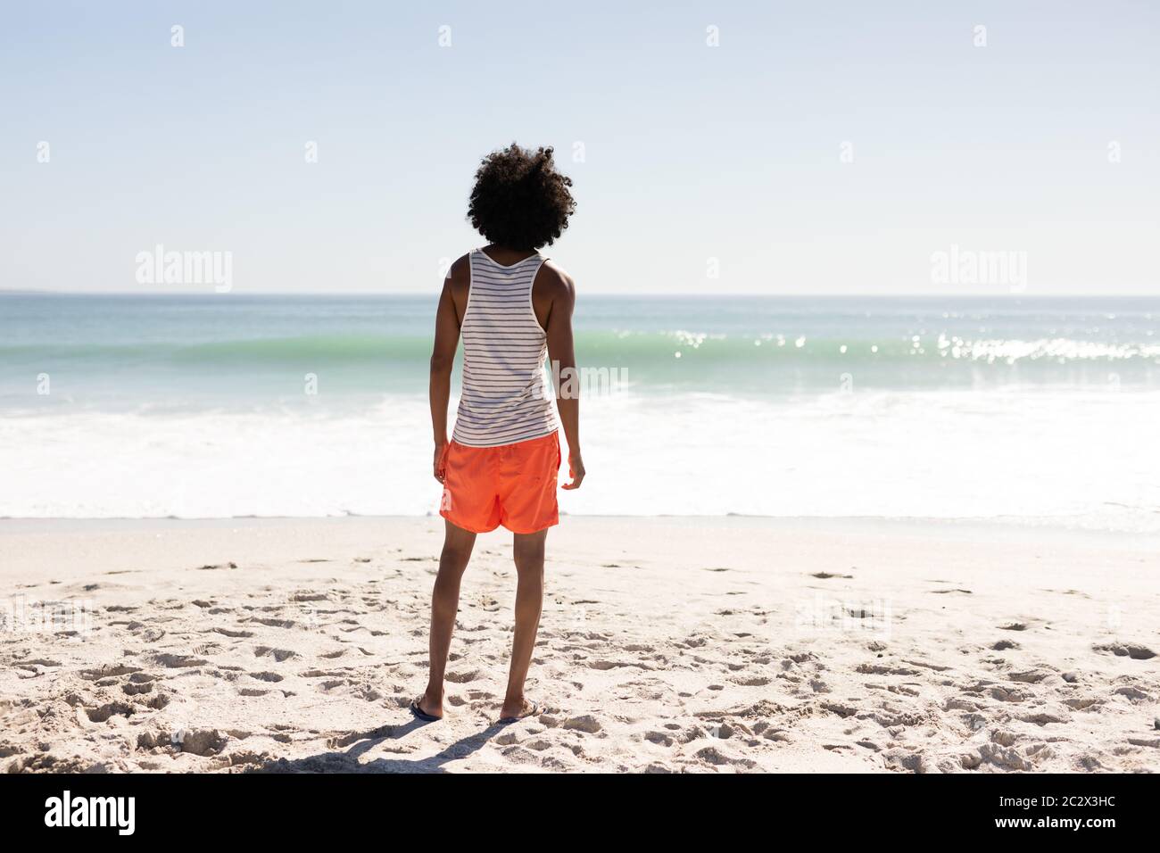 Junger Mann mit gemischter Rasse, der am Strand steht Stockfoto