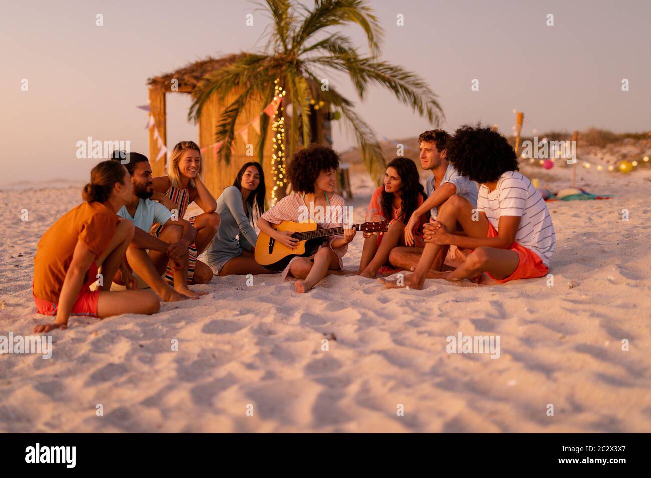 Multiethnische Gruppe von Männern und Frauen, die am Strand sitzen Stockfoto