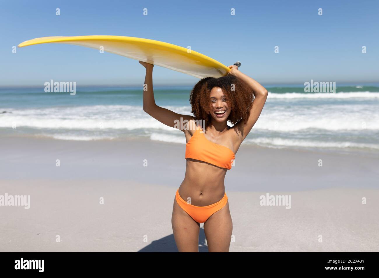 Mixed Race Frau hält ein Surfbrett am Strand Stockfoto
