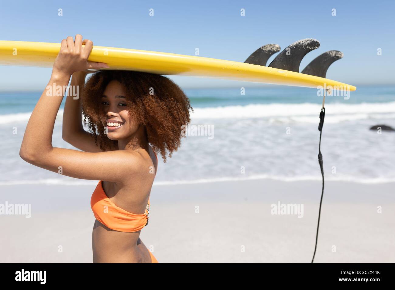 Mixed Race Frau hält ein Surfbrett am Strand Stockfoto