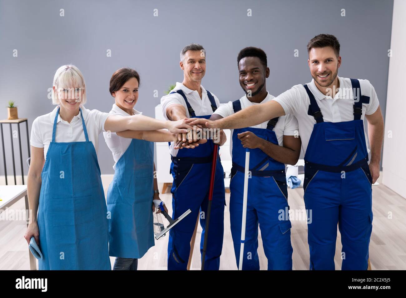 Portrait Von Fröhlichen Verschiedenen Hausbetern Im Büro Mit Reinigungsgeräten Stacking Hands Stockfoto