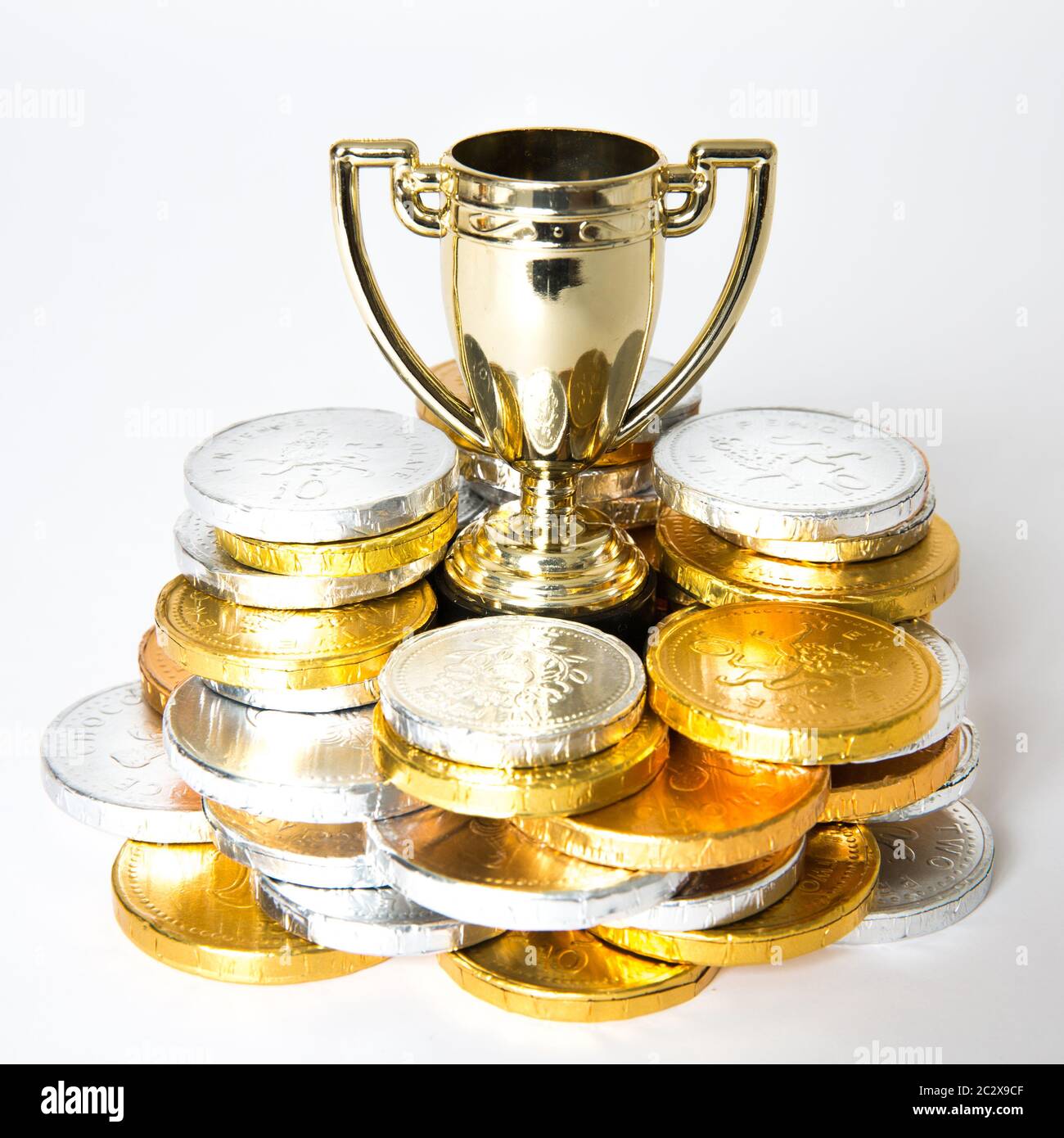 Ein Erfolg- oder Siegeskonzept mit einer Goldtrophäe oder einem Pokal, umgeben von Gold- und Silbermünzen in Form von Preisgeld Stockfoto