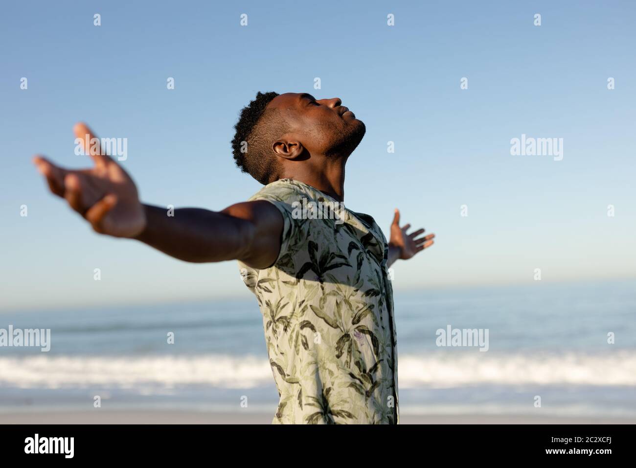 Ein afroamerikanischer Mann mit ausgestreckten Armen am Strand an einem sonnigen Tag Stockfoto