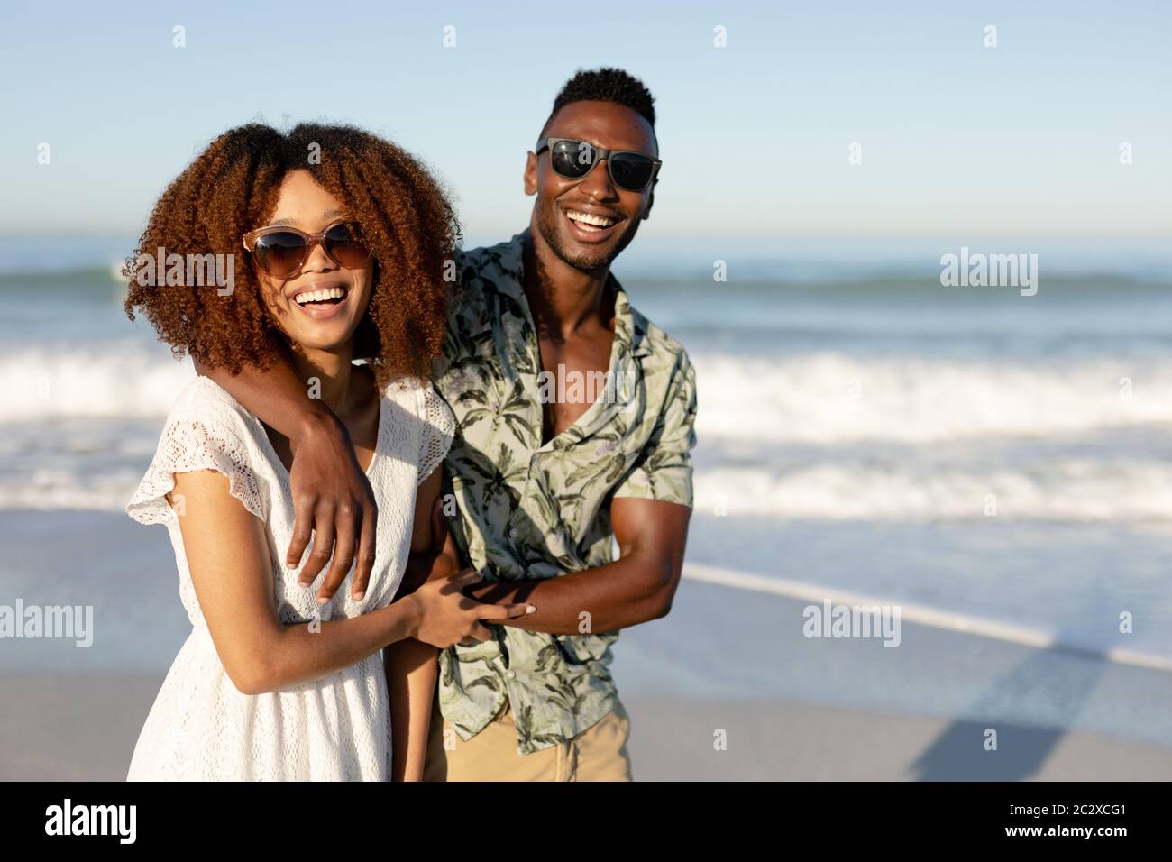 Ein gemischtes Rennpaar lachend und an einem sonnigen Tag in die Kamera am Strand schauend Stockfoto