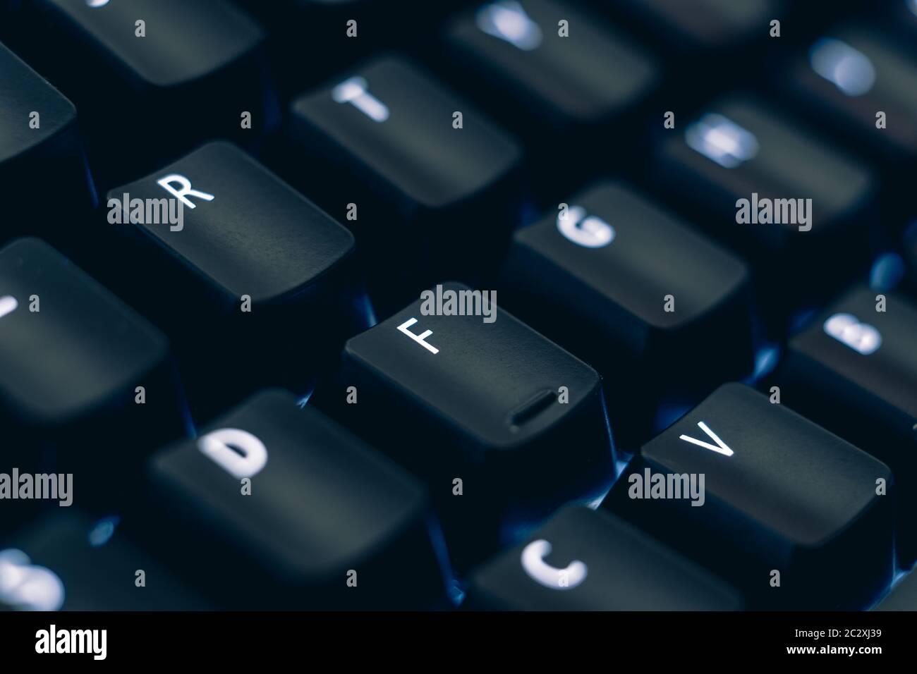 Makrofoto der mechanischen Tastatur. Konzentrieren Sie sich auf die Buchstaben R und F-Tasten. Die Buchstaben sind auf schwarzen Kunststoff-Tastenkappen geätzt, um die LED-Hintergrundbeleuchtung zu offenbaren. Stockfoto