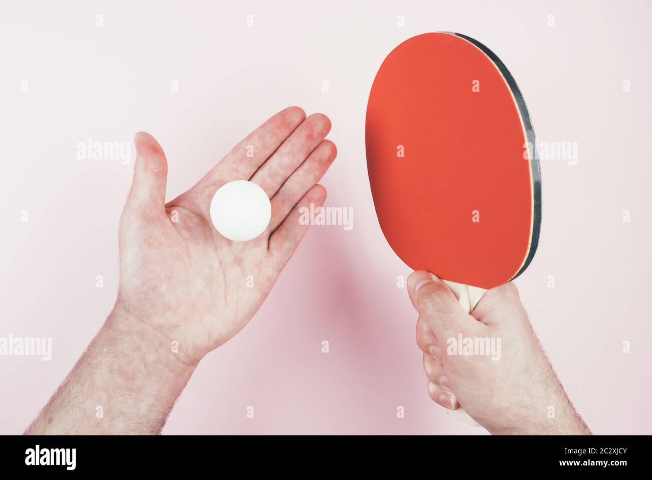 Oben Ansicht der Person hält Tischtennis Ball in einer Hand und Schläger in der anderen vor rosa Hintergrund Stockfoto