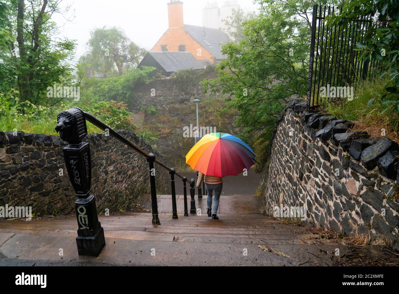 Frau mit buntem Regenschirm steigt am Regentag in Calton Hill, Edinburgh, Schottland, Großbritannien, die Treppe hinab Stockfoto