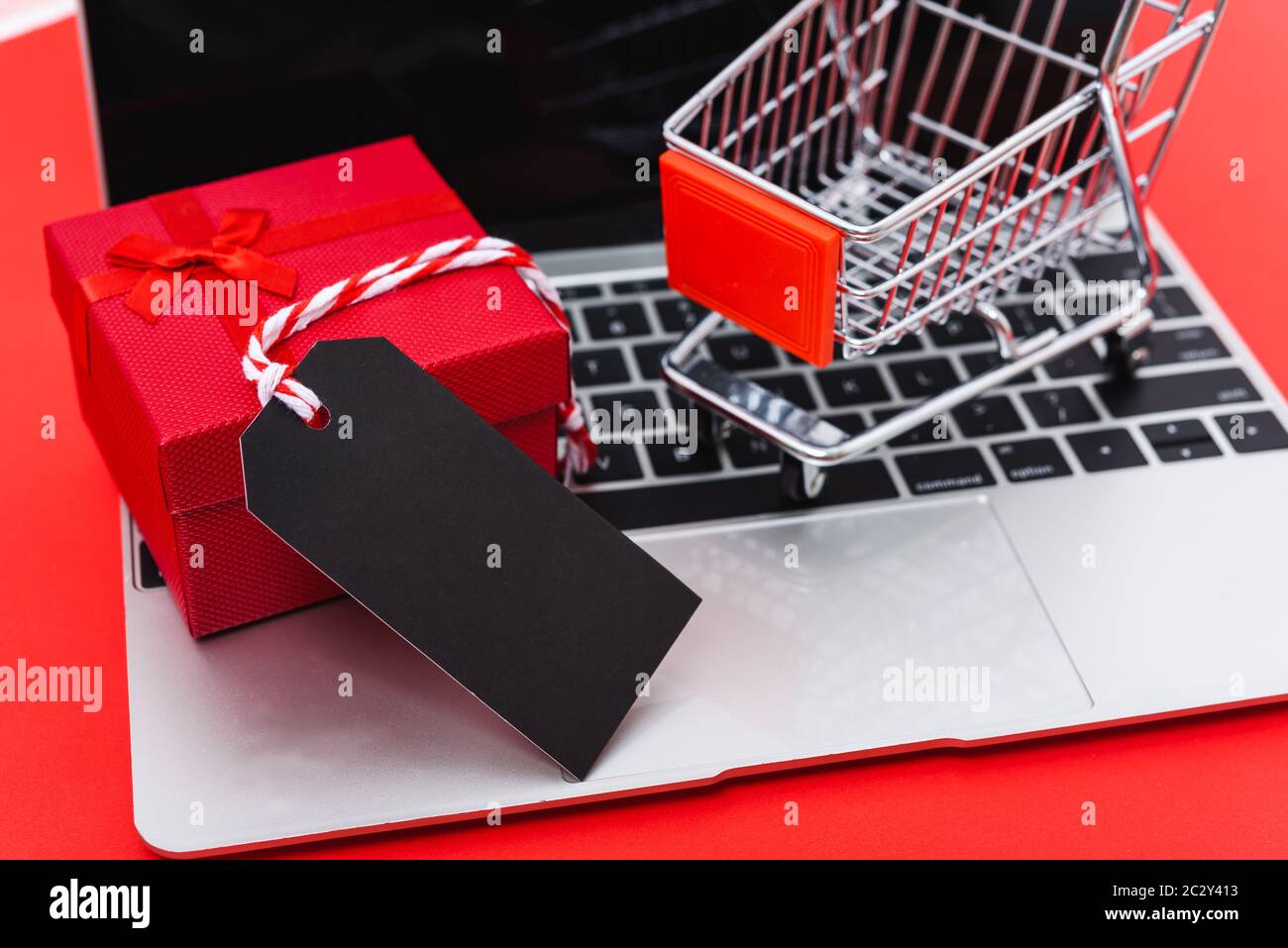 Internet online shopping Marketing, Ansicht von oben Arbeitsbereich mit leeren schwarzen Tag, Geschenkbox und Warenkorb auf Laptop auf rotem Hintergrund und ha Stockfoto