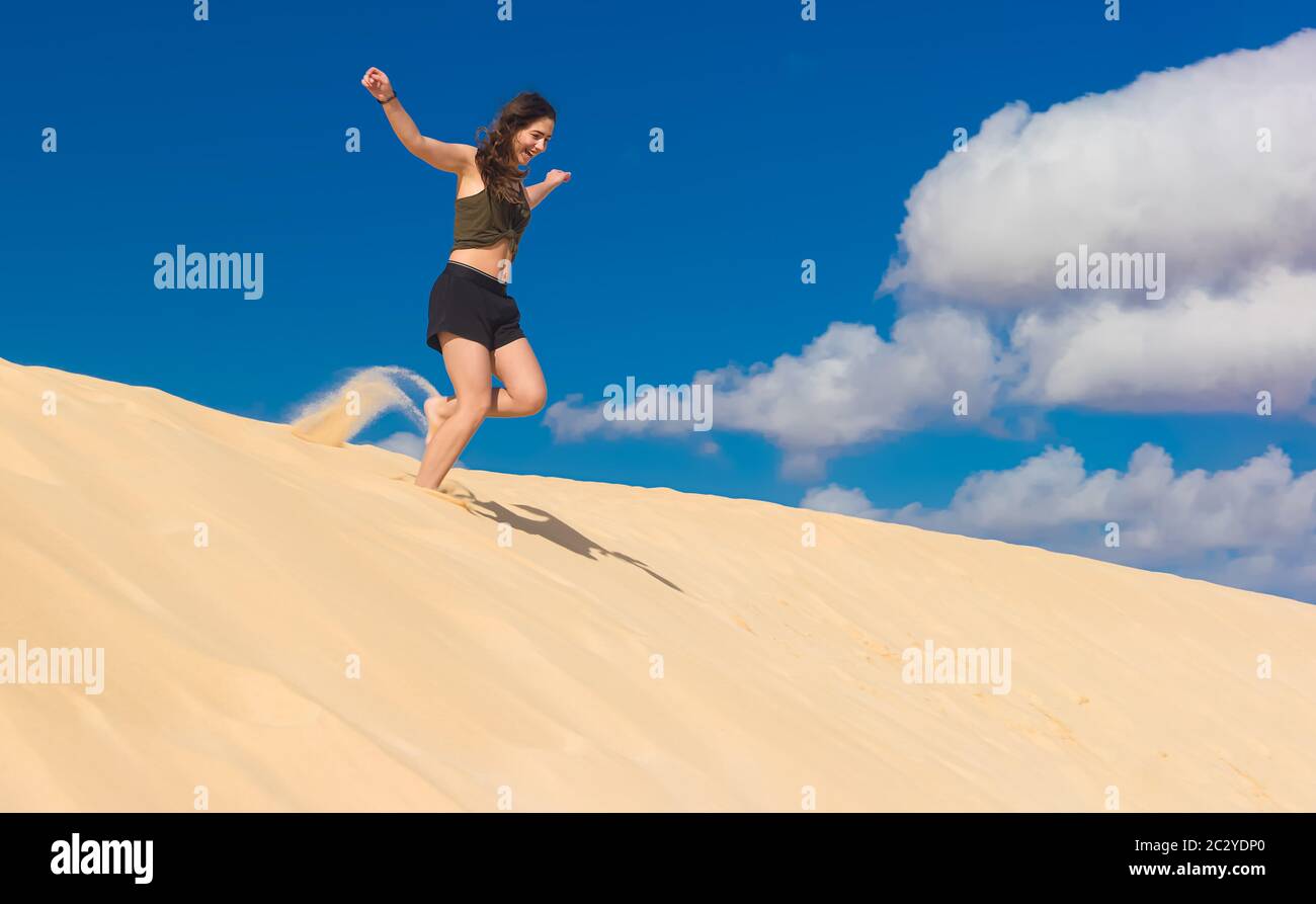 Ein Mädchen rennt im Sommer von einer Sanddüne voller Lebensfreude und wirbelt Staub auf Stockfoto