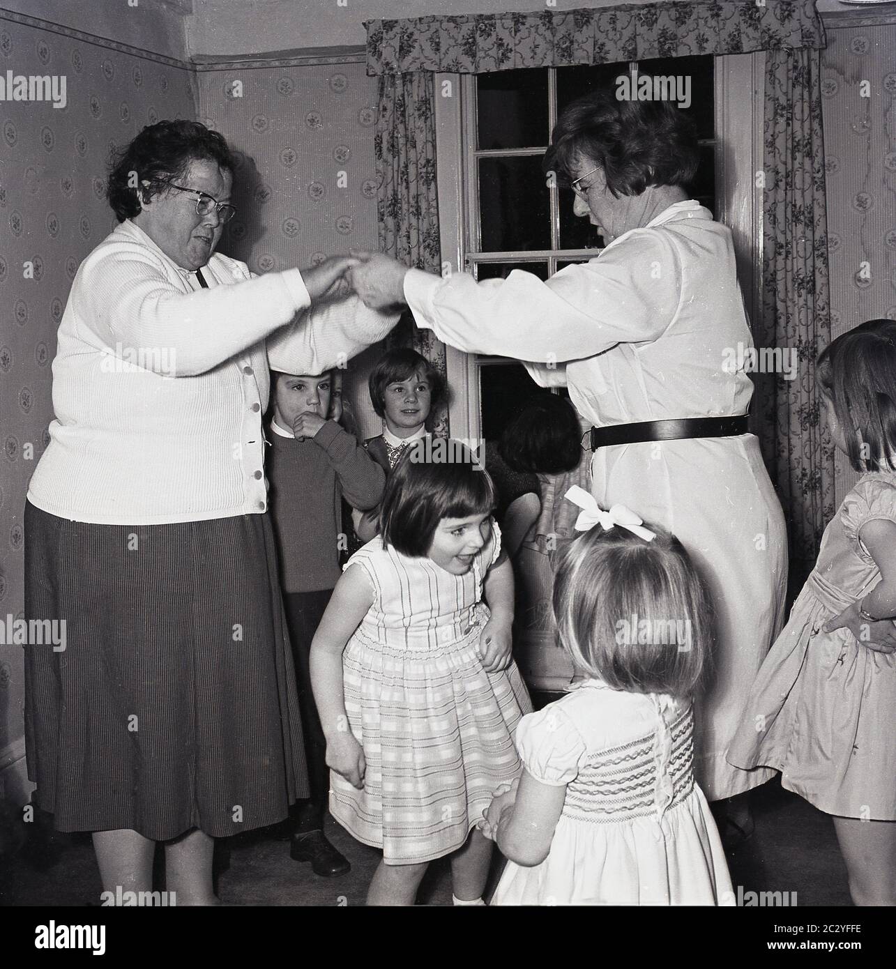 1960er Jahre, historisch, in einem Raum bei einer Kindergeburtstag, aufgeregt Jugendliche Spaß haben, ein Spiel unter den Armen von zwei Damen, England, Großbritannien gehen. Stockfoto