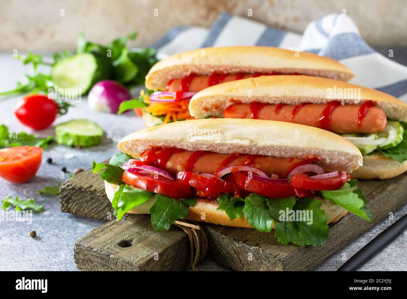 Fast Food. Hot Dog mit Grillwurst und frischem Gemüse auf einem hellen Stein- oder Schiefertisch. Stockfoto