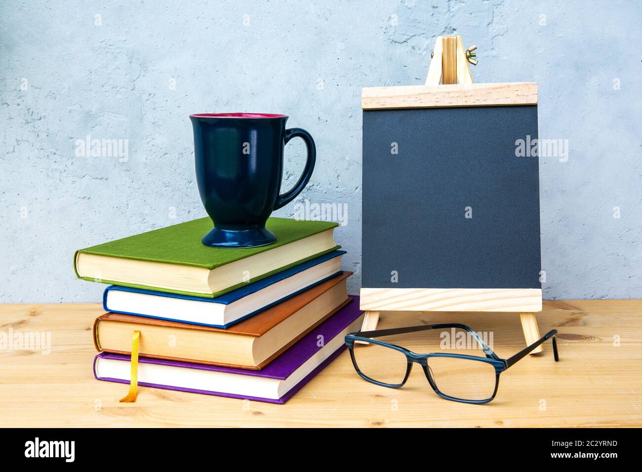 Kleine Tafel auf Holztisch mit Büchern, Becher und Brillen mit grauem Hintergrund Stockfoto