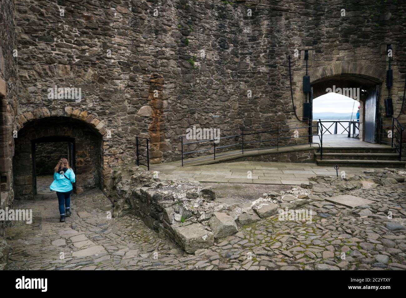 Eine weibliche Touristin spaziert über den felsigen Fuß des Blackness Castle, geformt wie ein Schiff, während sie Filmorte des beliebten Zeitfahrens Outlander tv besucht Stockfoto