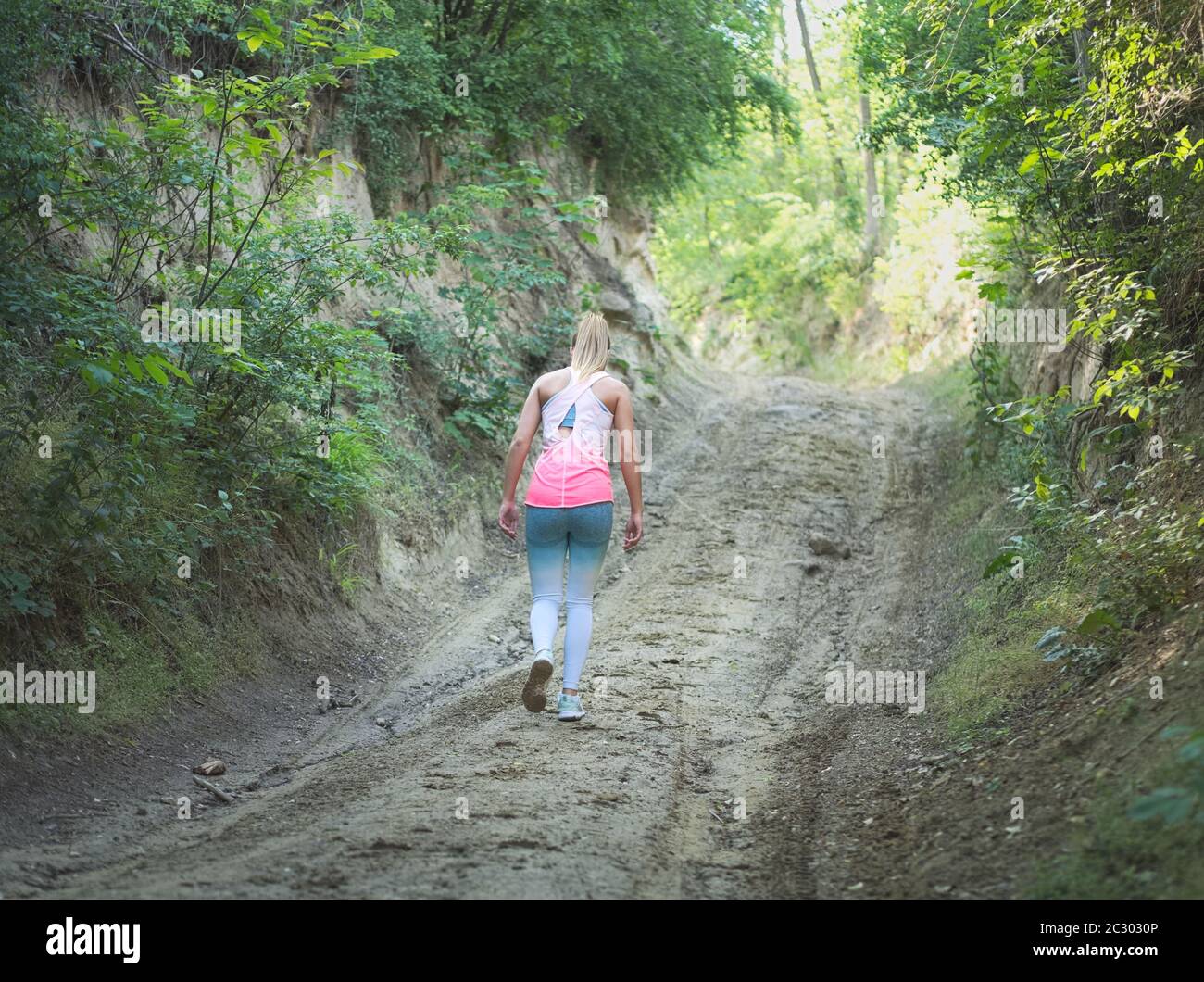 Junge Blonde kaukasische Frau zu Fuß in Wald auf einer Feldstraße Stockfoto