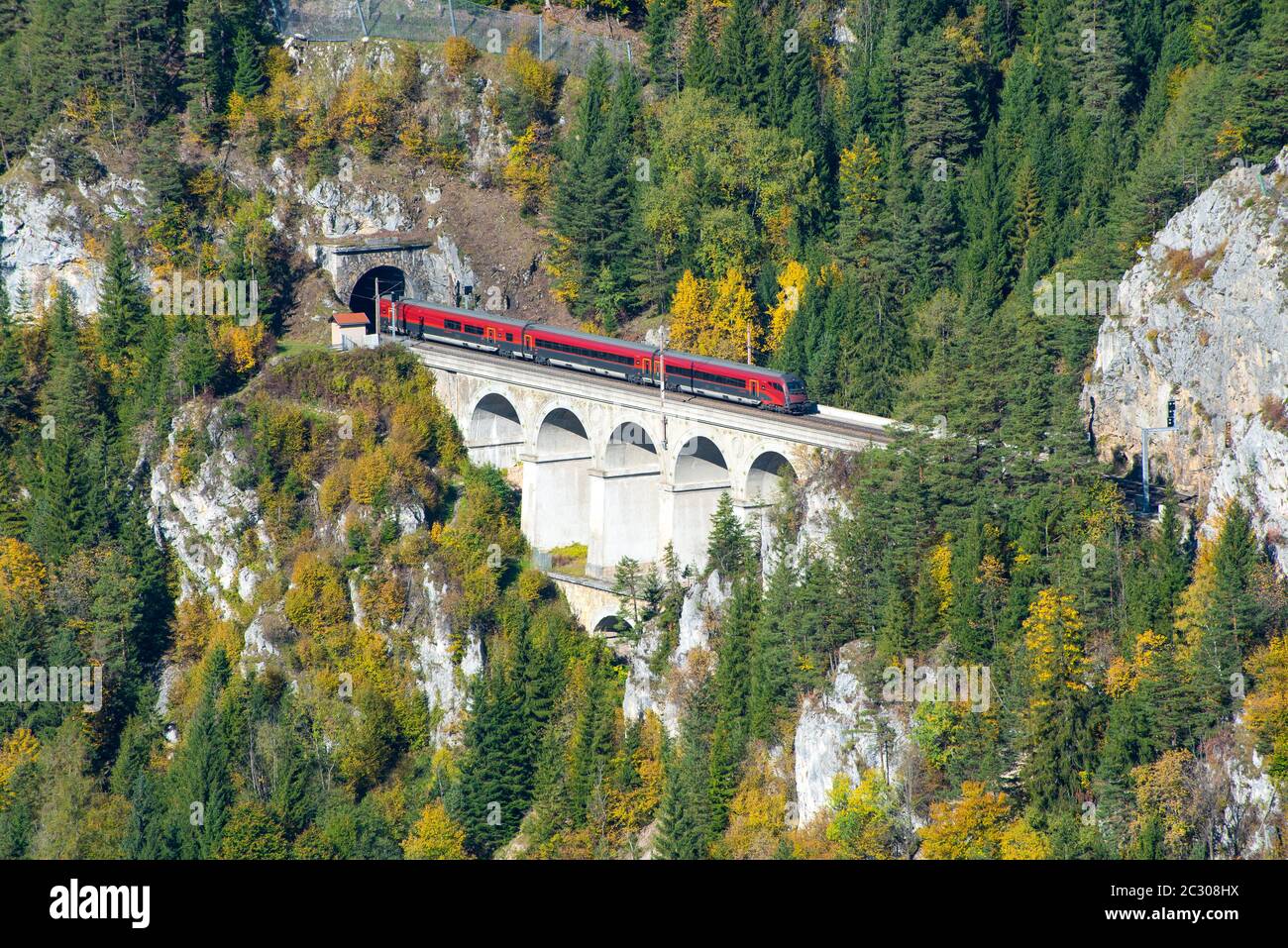 Roter Zug auf einem Viadukt zwischen zwei Tunneln der Semmeringbahn. Die Semmeringbahn ist die älteste Bergbahn Europas und gehört zur UNESCO-Welt Stockfoto