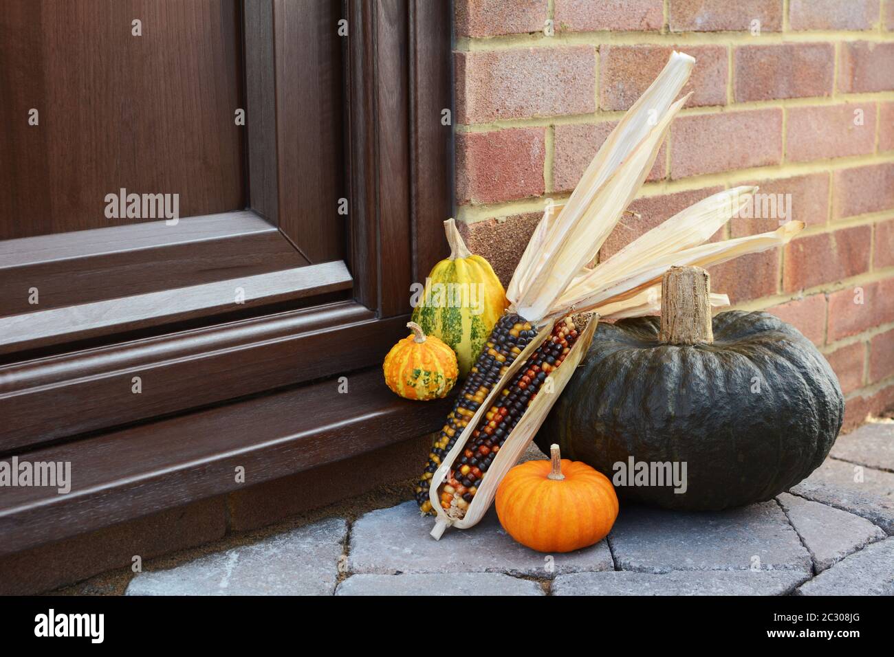 Große grüne Squash und dekorative Kürbisse mit bunten indischen Mais als Danksagung Dekoration auf einer Türschwelle Stockfoto