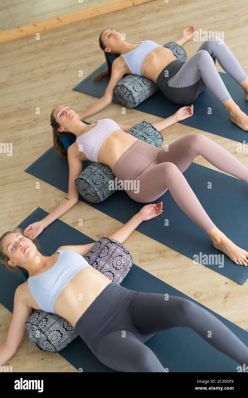 Restorative Yoga mit Polstern. Gruppe von drei Jungen sportlich attraktive Frauen in Yoga Studio, liegen auf Kissen Polstern, Stretching und Entspannung Stockfoto