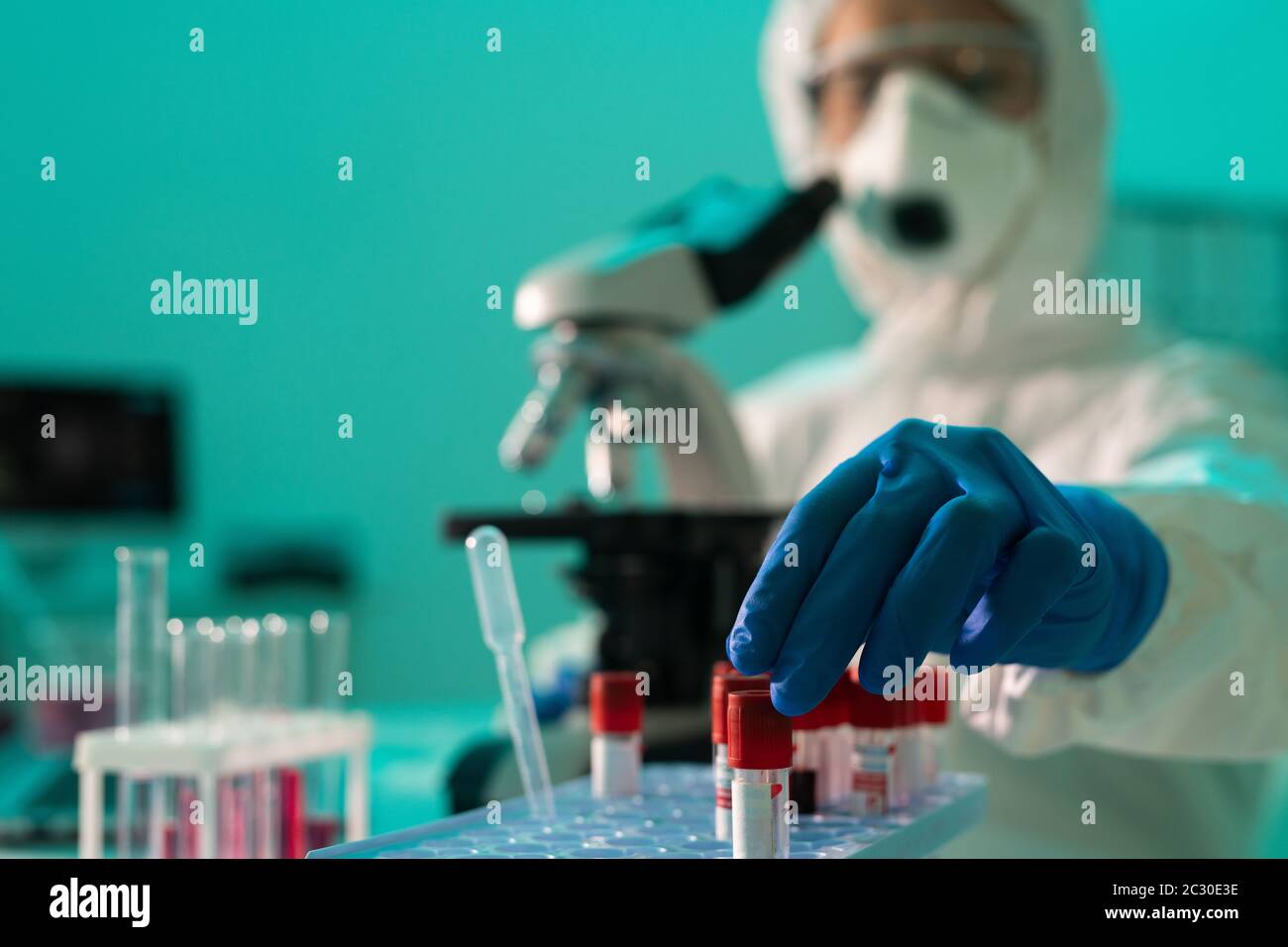 Nahaufnahme eines Laborarbeiters in Schutzkleidung, der das Reagenzglas in das Rack einlegt, während er das Blut von Coronavirus-Patienten untersucht Stockfoto