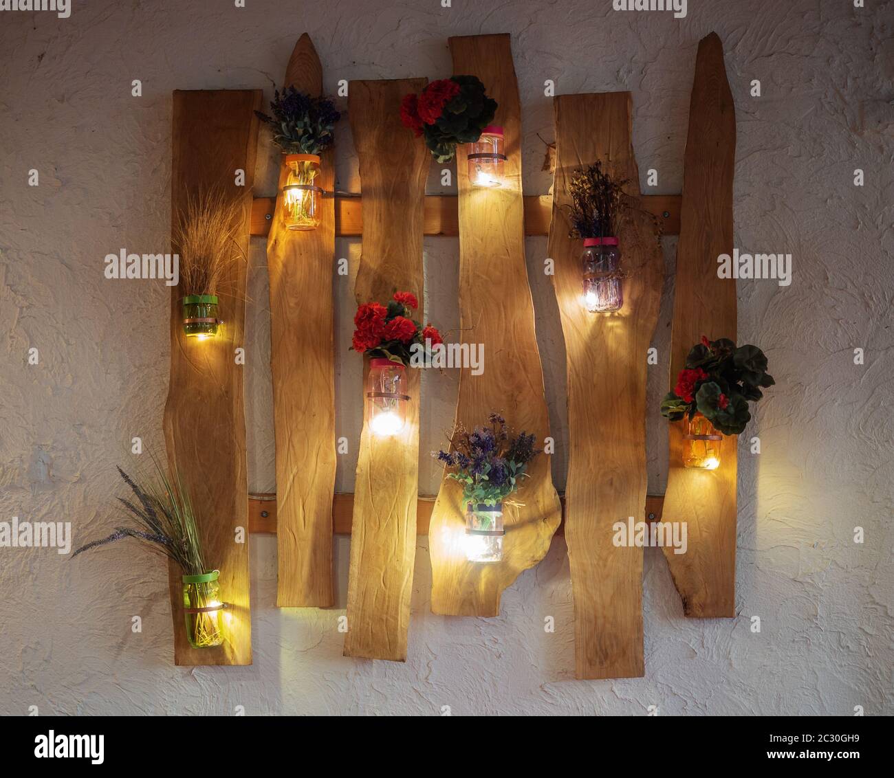 Dekorative Blumen in Glasvasen mit Lichtern an der Wand Stockfoto