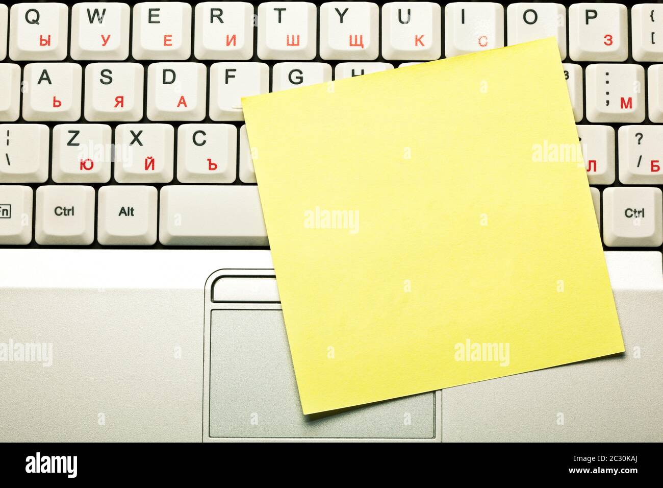 Draufsicht auf eine leere leere gelbe Haftnotiz auf grauem Laptop-Tastatur-Trackpad. Stockfoto