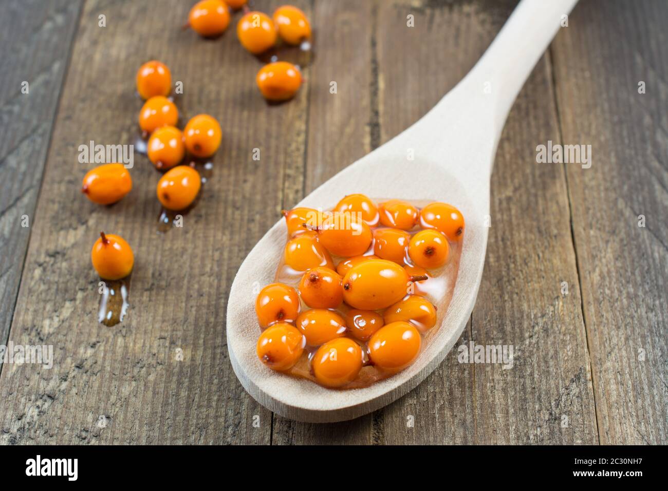 Nahaufnahme der Sanddornbeeren mit Honig auf Holzlöffel. Ausgezeichnetes Mittel gegen Kälte, hoher Gehalt an Vitamin C Stockfoto