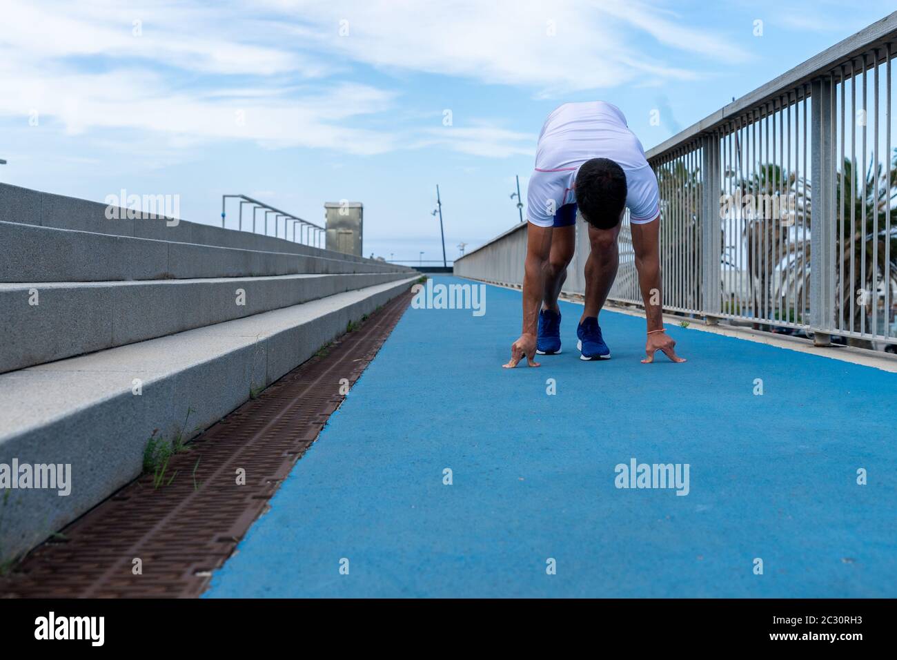 Junger Läufer in blauer Hose und weißem T-Shirt läuft in der Sonne auf blauer Bahn. Motivationskonzept, Karriere Stockfoto