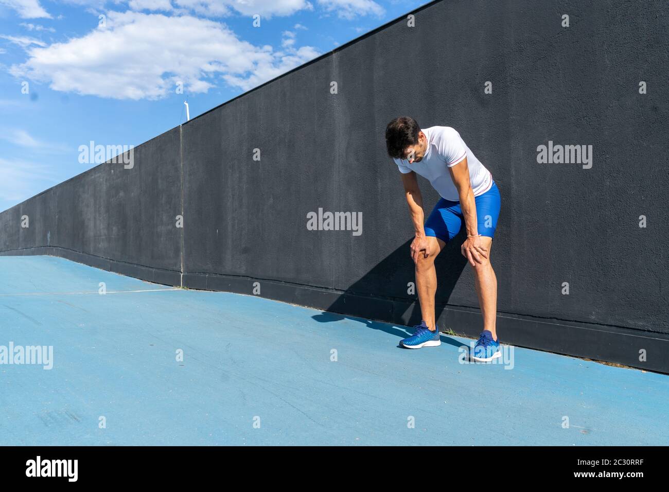 Junger Laufmann in blauer Hose und weißem Hemd, der sich in voller Sonne auf der schwarzen Wand ausruhte und erholte. Motivationskonzept, Karriere Stockfoto