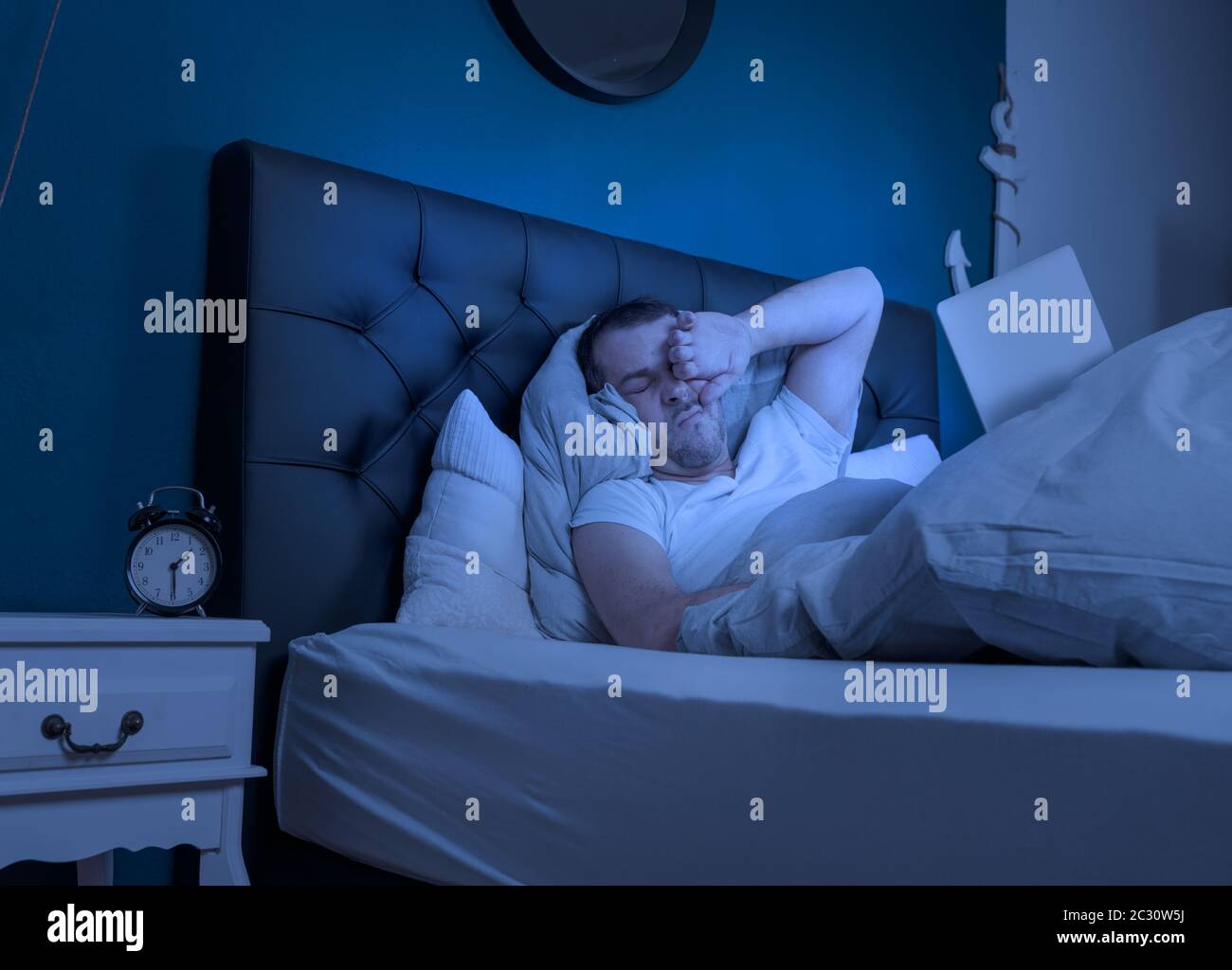 Ein übermüder Mann arbeitet in der späten Nacht auf seinem Laptop Stockfoto