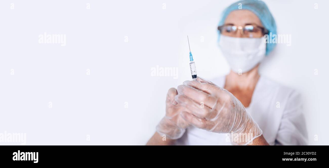 Ältere ältere Frau Arzt oder Krankenschwester mit Spritze in einem weißen medizinischen Mantel, Handschuhe, Gesichtsmaske tragen persönliche Schutzausrüstung isoliert. Gesundheitswesen Stockfoto