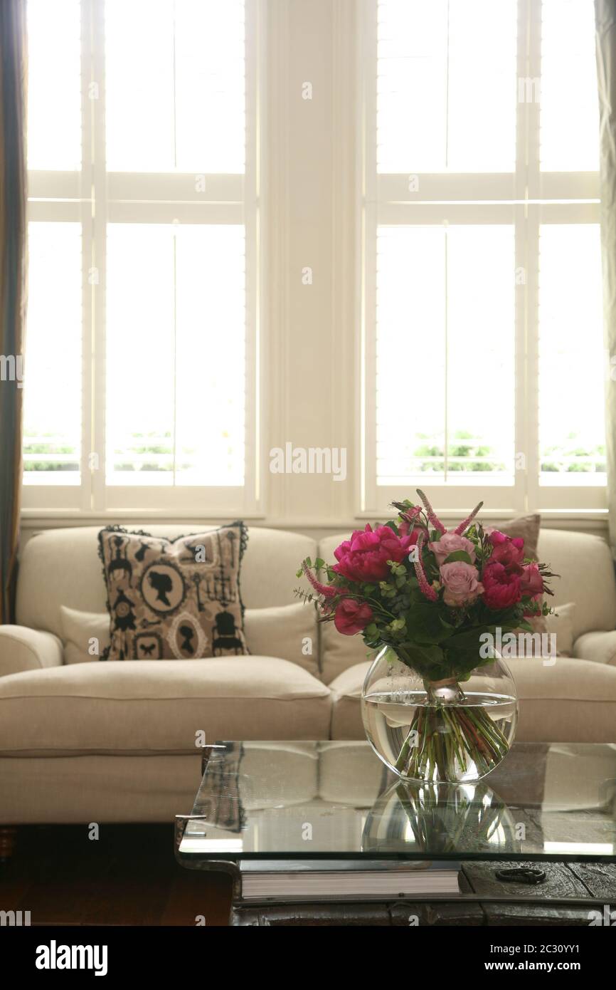 Blick auf einen Couchtisch und Blumen mit Sofa und Schiebefenstern im Hintergrund eines klassischen britischen Wohnzimmers Stockfoto