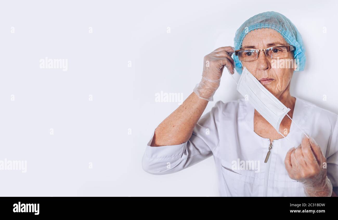 Ältere ältere Frau Arzt oder Krankenschwester in einem weißen medizinischen Mantel, Handschuhe, setzt auf Gesichtsmaske tragen persönliche Schutzausrüstung isoliert. Gesundheitswesen und Stockfoto