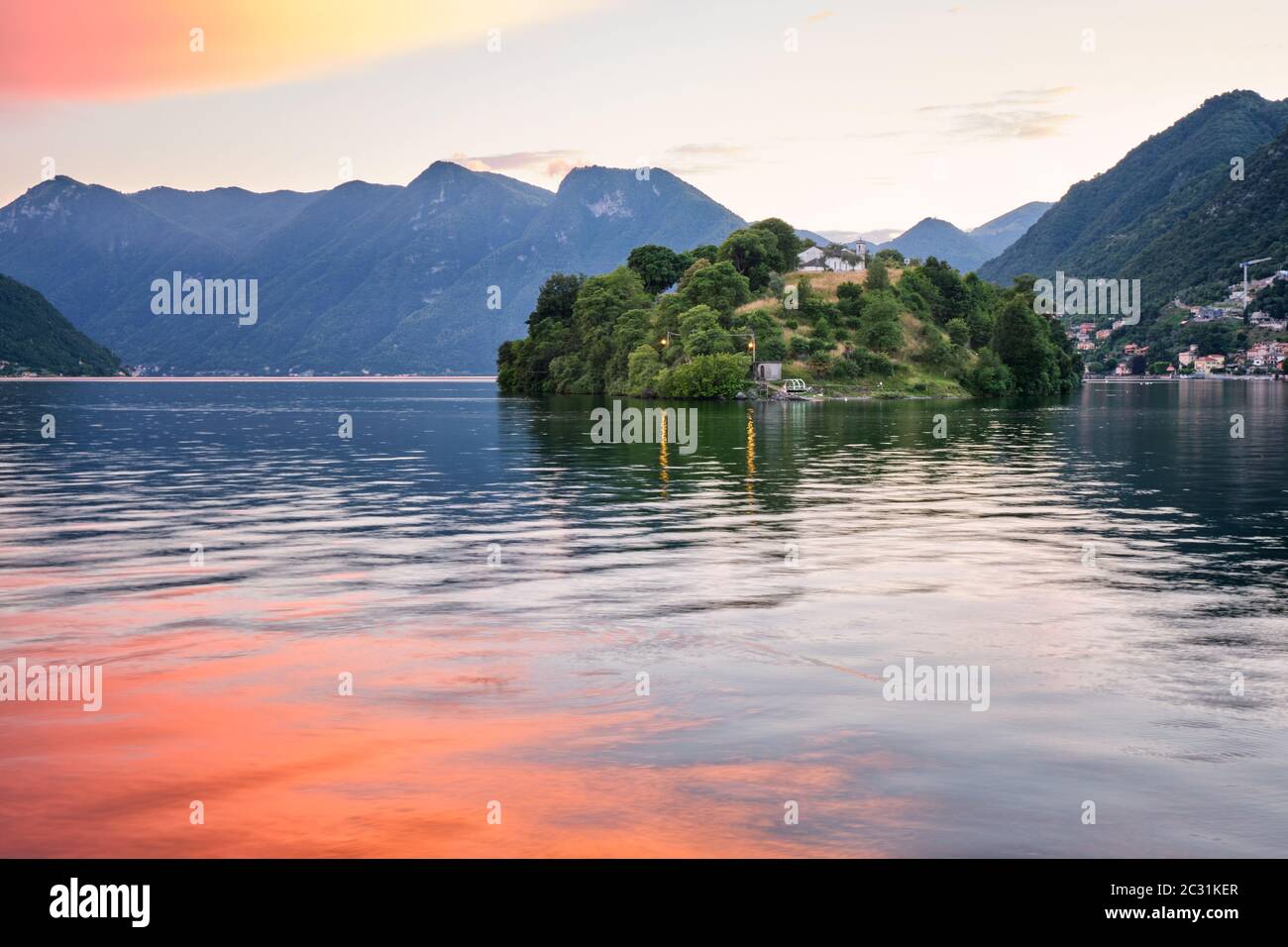 Isola Comacina bei Sonnenuntergang umgeben von orangen Wolken und bunten Wasserspiegelungen, Comer See, Italien Stockfoto