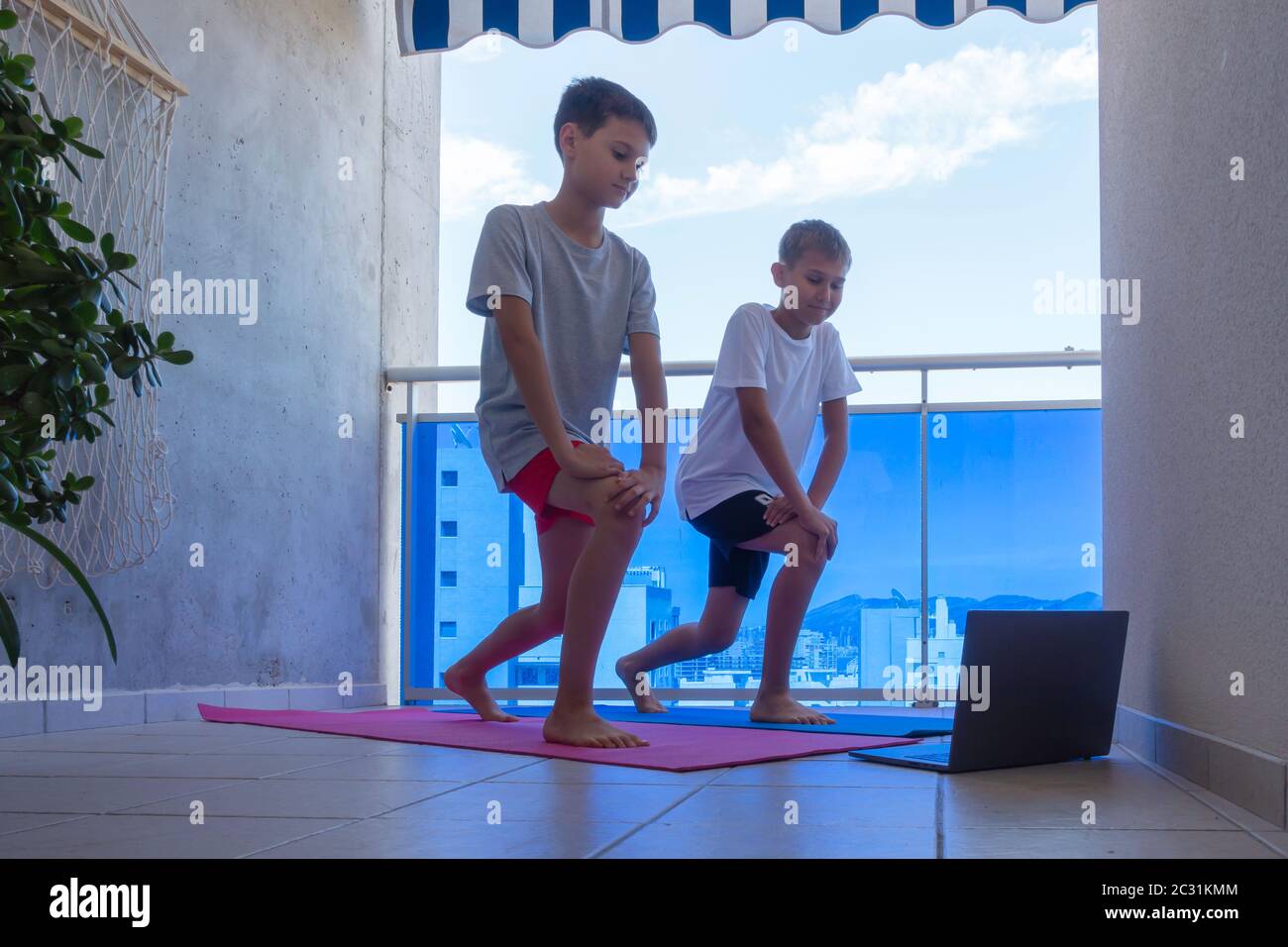 Jungs mit Laptop-Computer, die Sportübungen auf dem Balkon machen. Sport, gesunder Lebensstil, aktive Freizeit zu Hause Stockfoto