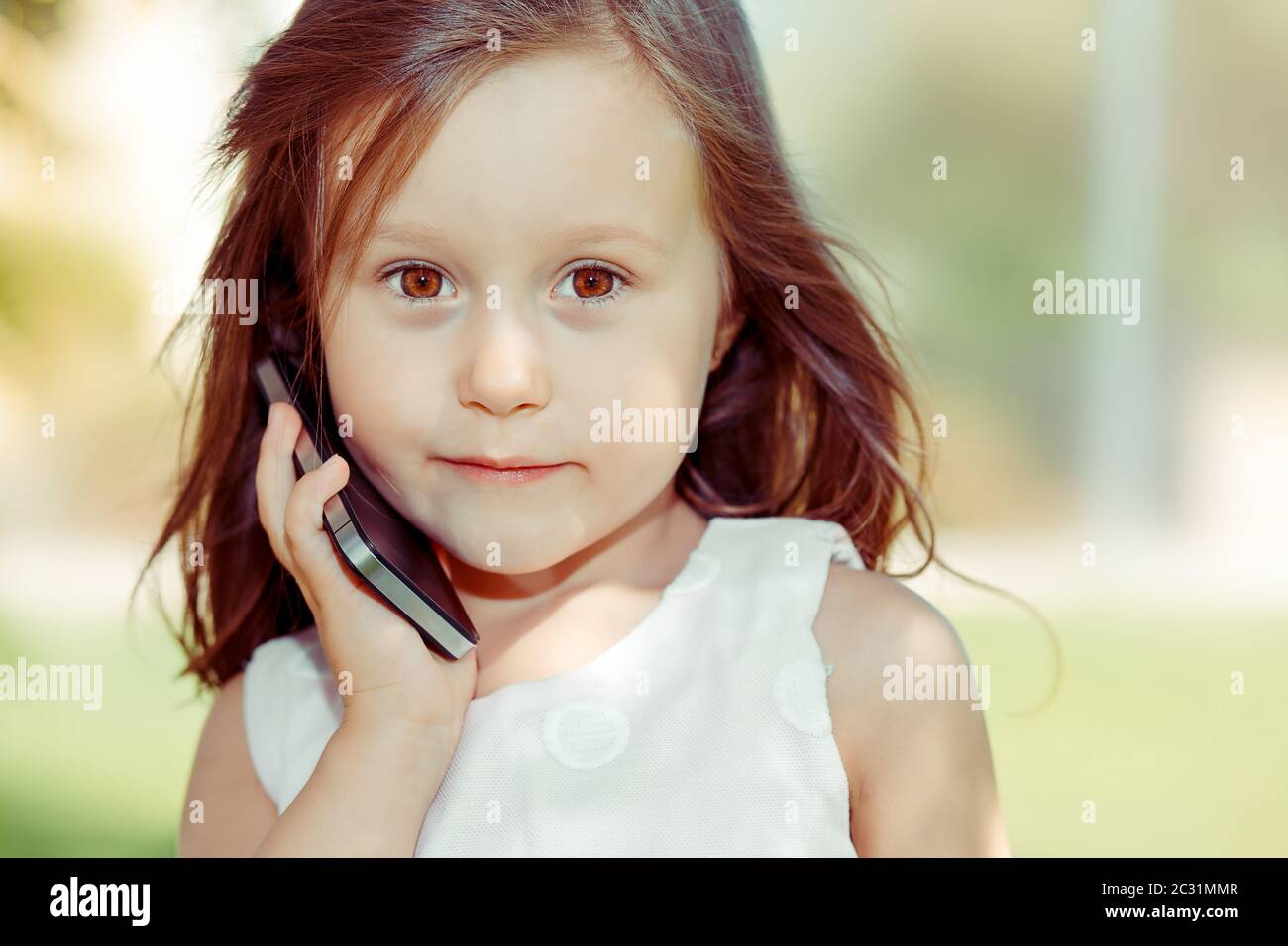 Kind mit Smartphone. Nahaufnahme Porträt von ziemlich ernst lustige Mädchen Kind hält Handy sprechen mit ihrer Mutter, Papa Familie isoliert grünen Bäumen im Freien Stockfoto