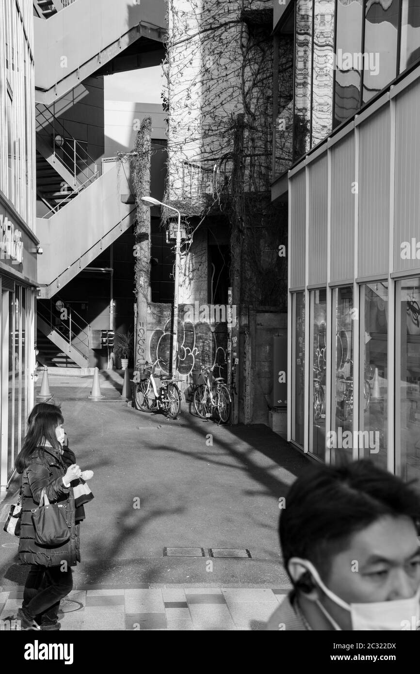 Blick auf Gebäude und Menschen mit Gesichtsmasken, die auf einer Straße neben dem Bahnhof Harajuku spazieren. Schwarzweiß-Foto. Stockfoto