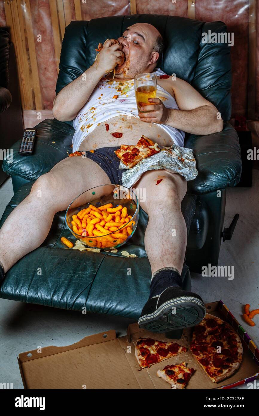 Fat couch potato Essen einer riesigen Hamburger und Fernsehen. Grelle Beleuchtung aus dem Fernsehen beleuchtet die dunklen Zimmer. Stockfoto