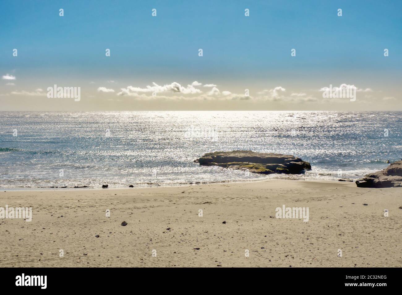 Strandabschnitt mit ruhigem silbernem Atlantik im Gegenlicht mit einem großen Lavastein am Wasserrand auf der Kanarischen Insel Teneriffa. Konzentrieren Sie sich auf Th Stockfoto