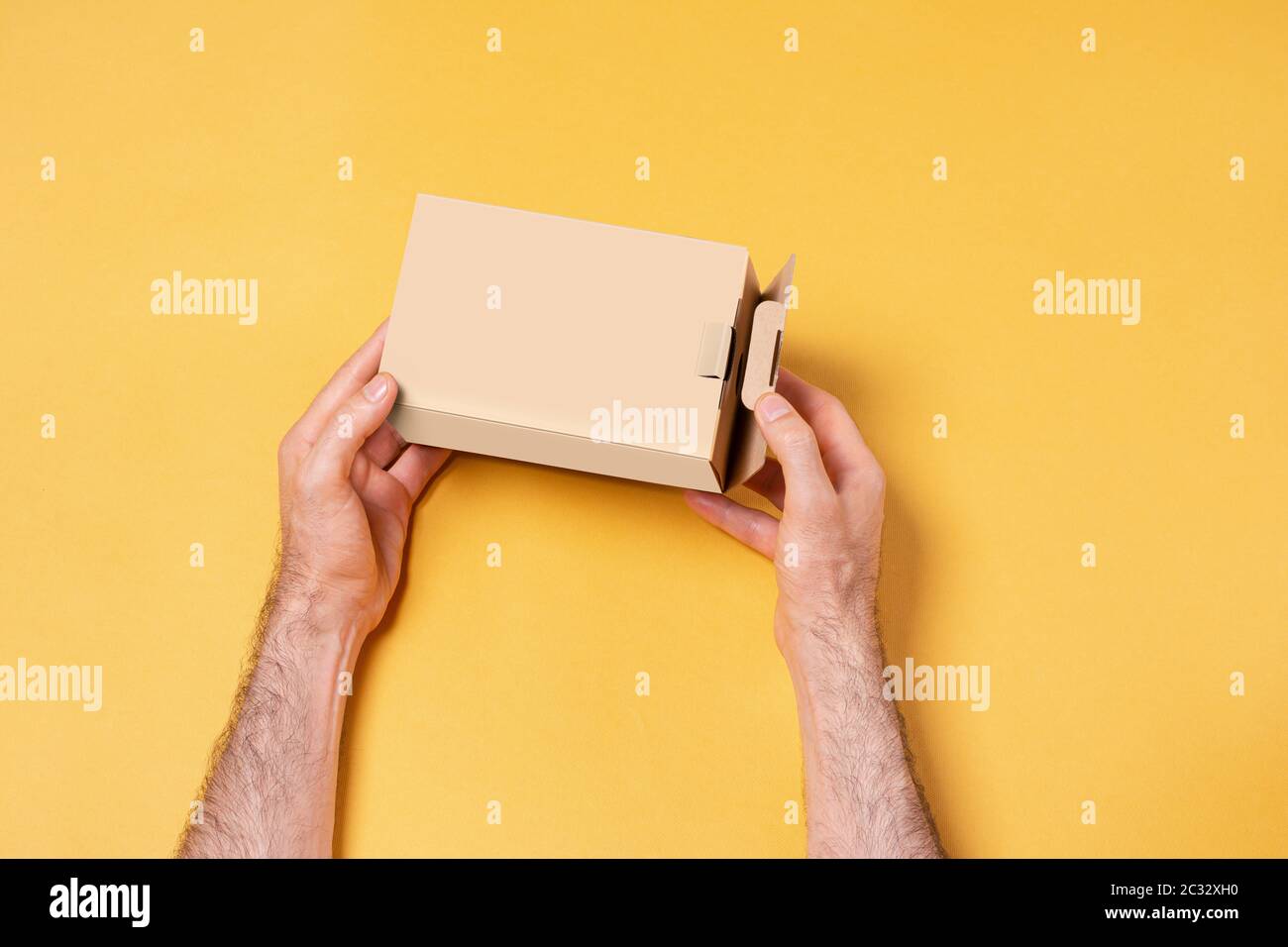 Männliche Hand hält eine kleine Box vor dem gelben Hintergrund, Modell-up-Serie Vorlage bereit für Ihr Design-Auswahl-Pfad enthalten Stockfoto