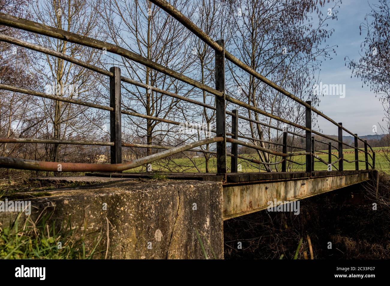 Kleine Eisenbrücke über den kleinen Fluss und eine grüne Wiese Stockfoto
