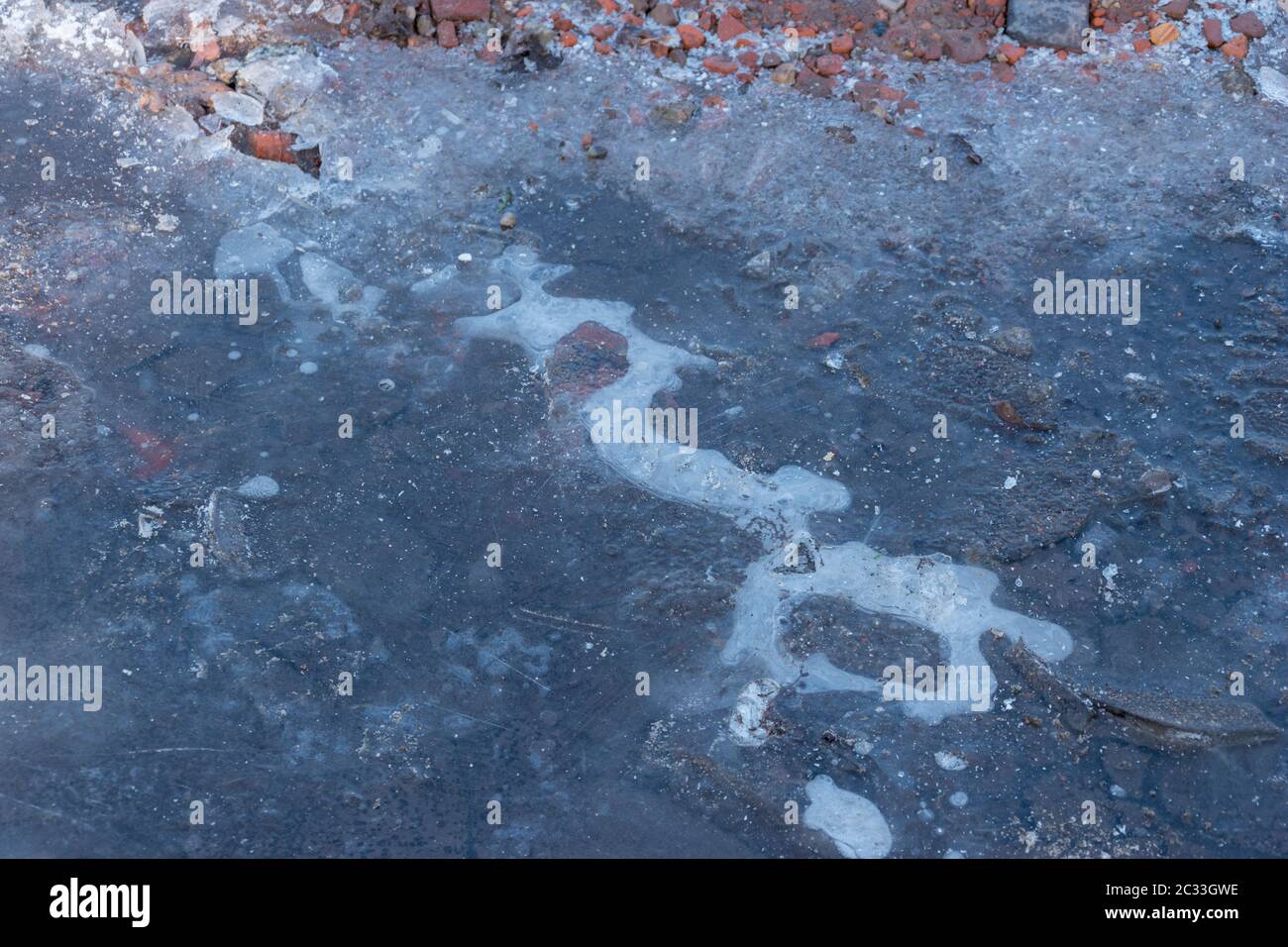 Gefrorenen Pfütze mit gebrochenem Eis. Eiskruste auf gefrorenen Pfütze. Winter Hintergrund. Gefrorenen Pfütze auf der Straße. Im Januar. Gefrorenen Pfütze und Schmutz der Straße in der Nähe Stockfoto