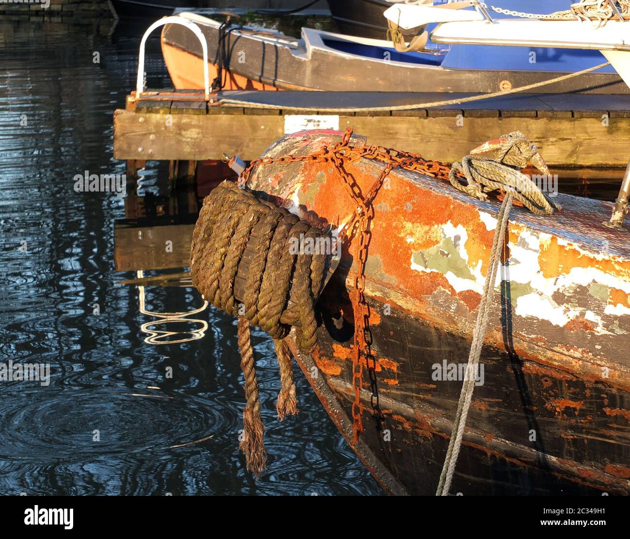 Der Bug eines alten rostigen Kanalbootes, das mit Seilen auf einem Steg mit Reflexen im dunklen Wasser festgemacht wurde Stockfoto