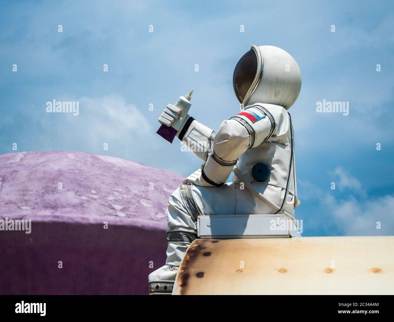 Ein Astronaut mit einem Schlauch von Lebensmitteln in der Hand sitzt auf dem Hintergrund des Himmels im Park von Russland Sotschi 06 22 2019 Stockfoto