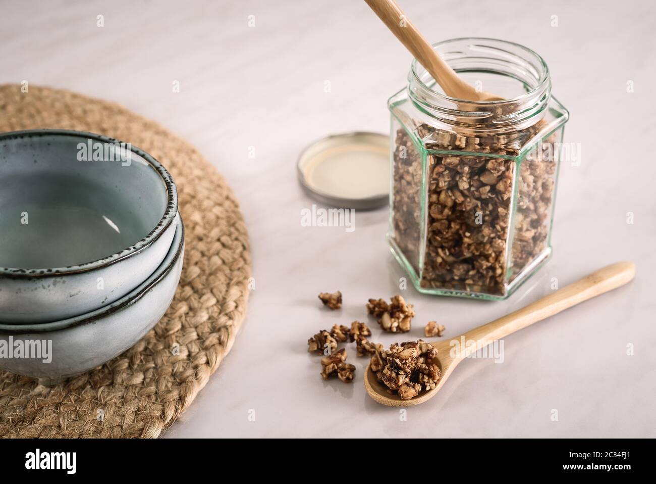 Hausgemachten gesunden und nahrhaften Frühstück Müsli in einem Glas und auf Löffel aus Holz mit blauer Keramik Schalen auf Marmor Küchentisch in frischen Morgen li Stockfoto