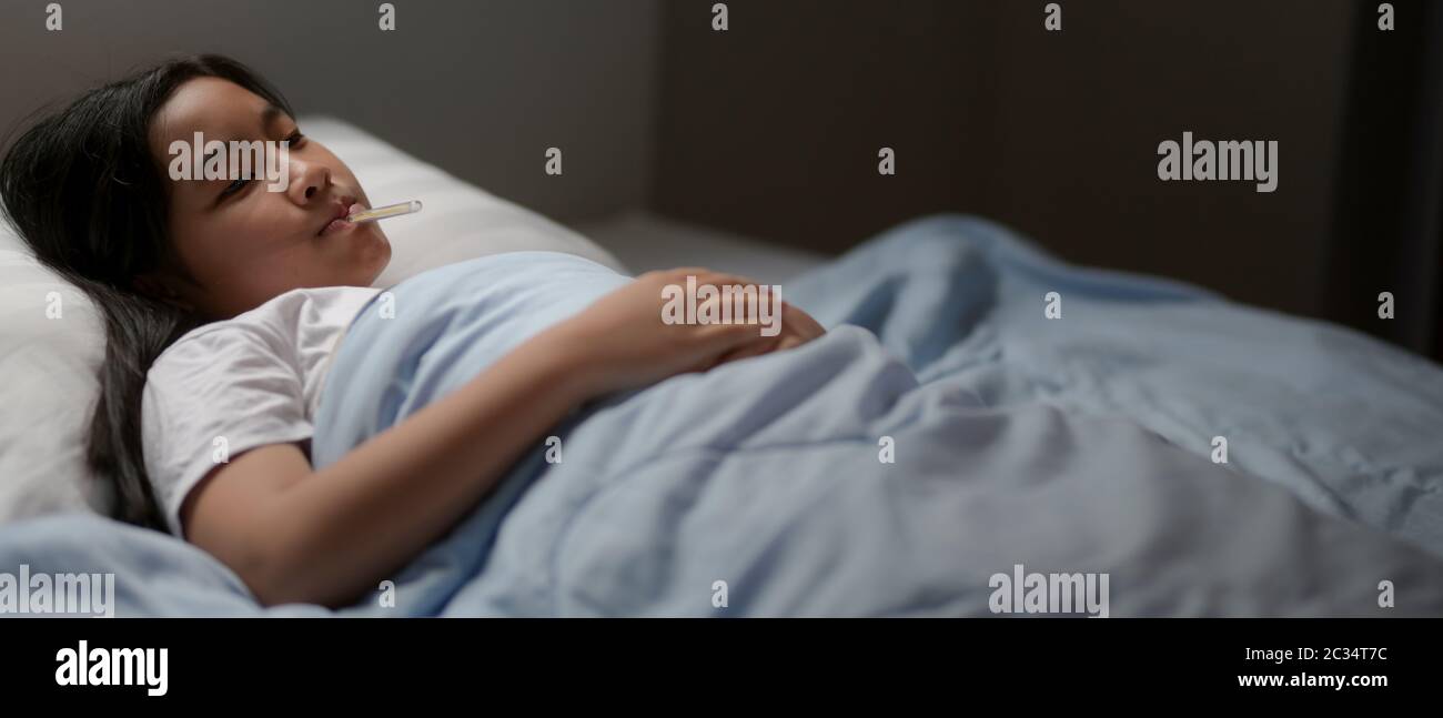 Zugeschnittene Aufnahme von kranken Mädchen auf dem Bett liegen, während die Temperatur mit Thermometer in den Mund nehmen Stockfoto