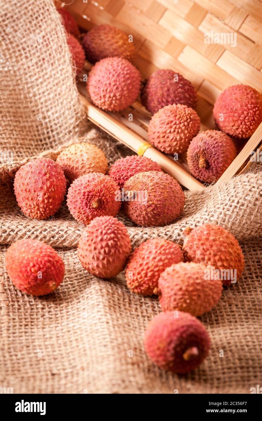 Hochwinkeliger Blick auf einen gekippten Obstkorb (Lichi) des Lycäumbaums (Litchi chinensis) auf grobem Sacktuchgewebe in einem eckigen Korb. Stockfoto