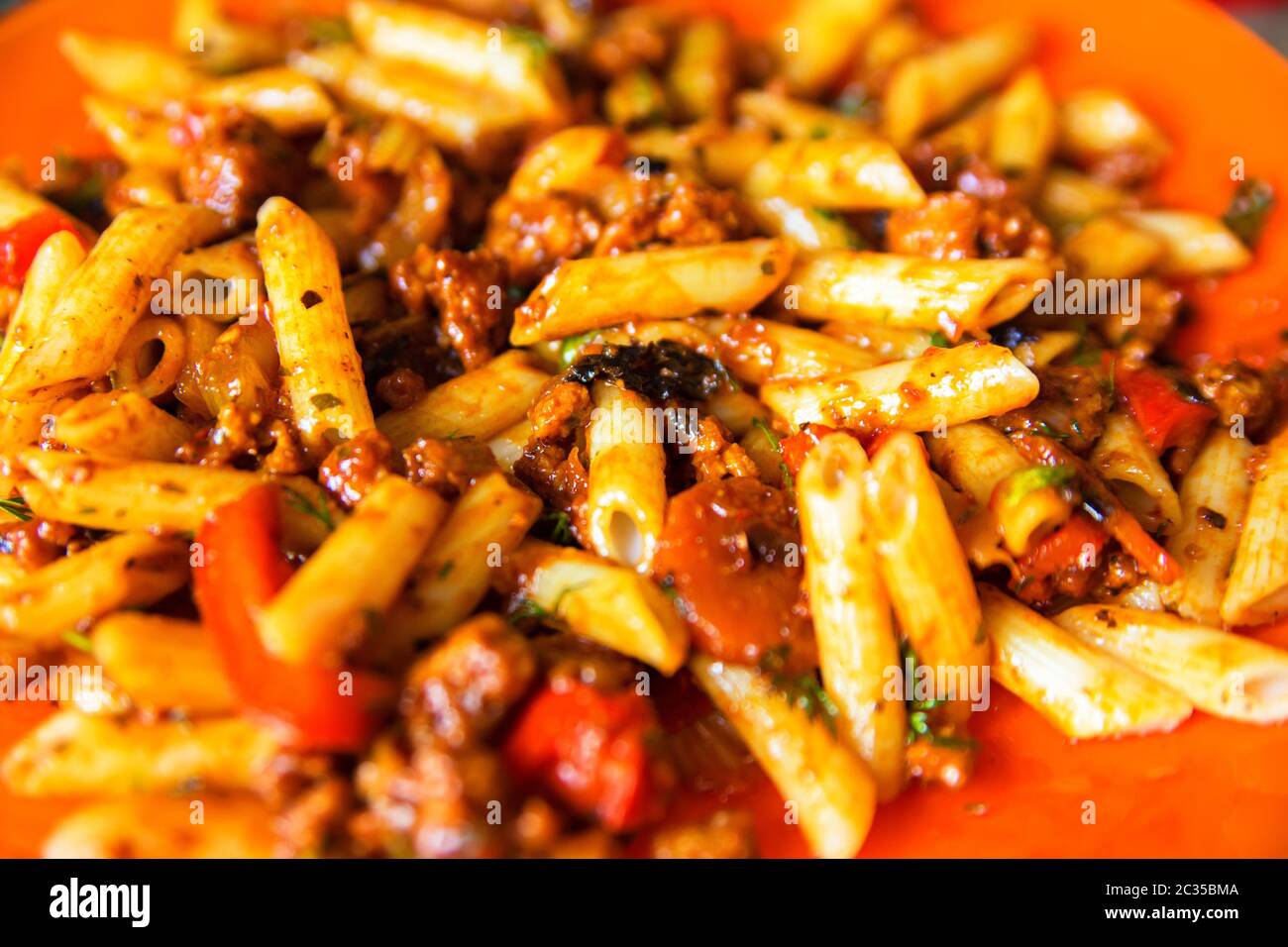 Italienische Nudelbolognese auf orangefarbenem Teller. Gehackte Platte mit köstlichen italienischen Makaroni mit Tomaten, frischen Basilikumblättern und geriebenem Parmesankäse Stockfoto